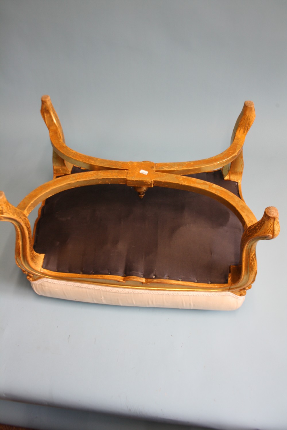 A mid-19th-century upholstered giltwood stool featuring carved cabriole legs, a serpentine seat rail, an X-shaped stretcher with a central finial, and a cream fabric top. View III