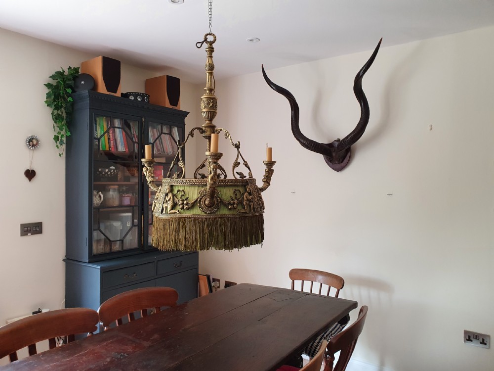 An Edwardian brass four-light chandelier featuring cast cherub figures, decorative swags, and a green fabric shade with hanging fringe.