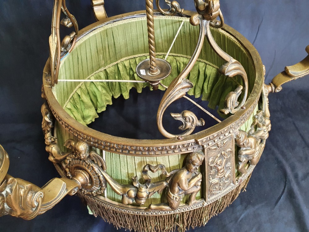 An Edwardian brass four-light chandelier featuring cast cherub figures, decorative swags, and a green fabric shade with hanging fringe. View IV