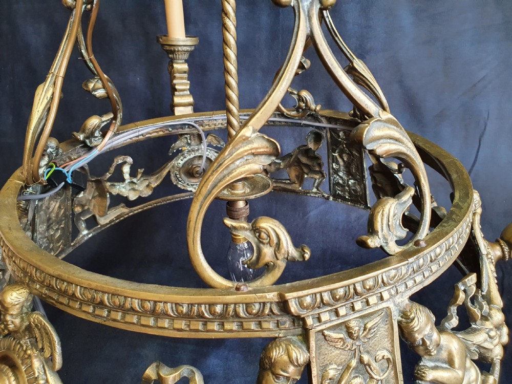 An Edwardian brass four-light chandelier featuring cast cherub figures, decorative swags, and a green fabric shade with hanging fringe. View XI