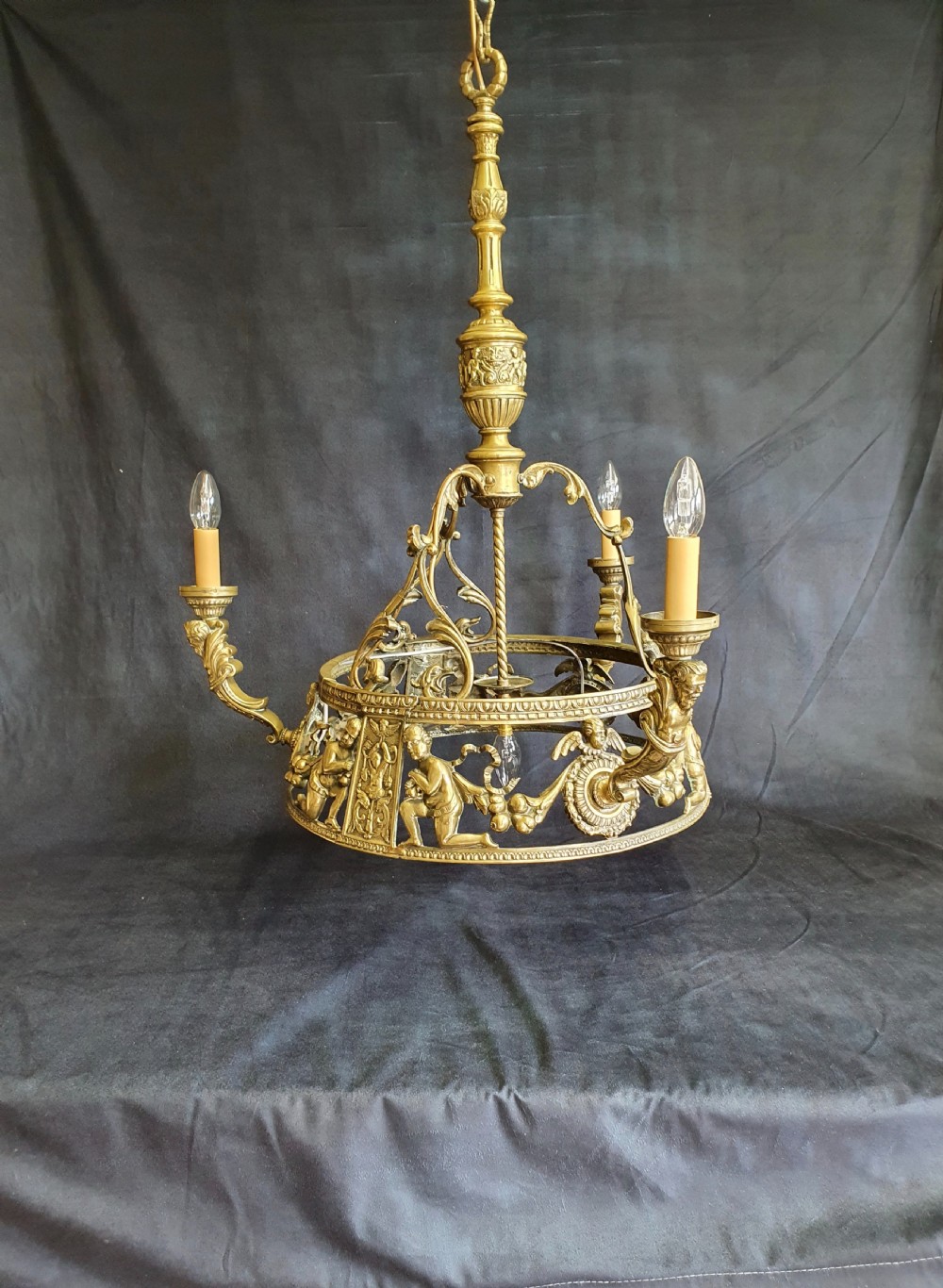 An Edwardian brass four-light chandelier featuring cast cherub figures, decorative swags, and a green fabric shade with hanging fringe. View XII