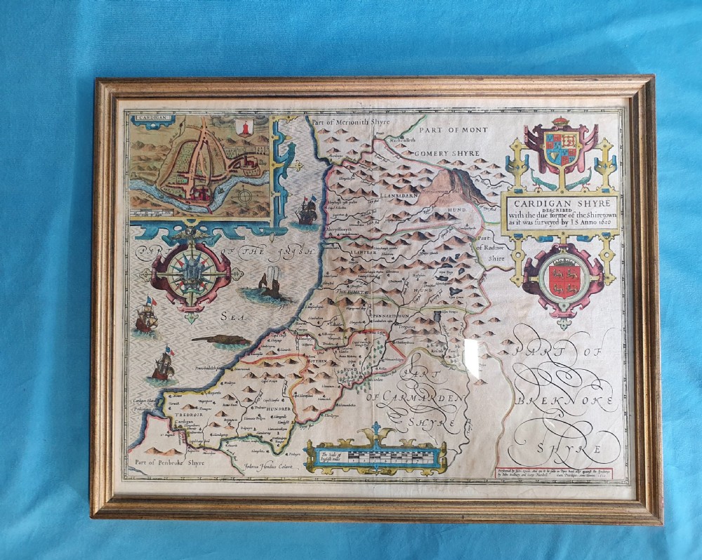 A framed 17th-century hand-coloured map of Cardiganshire featuring cartouches, heraldic coats of arms, and an inset town plan.
