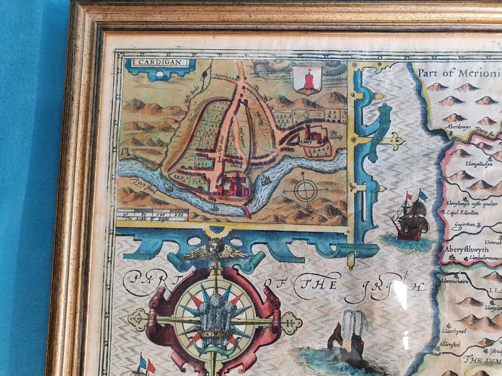 A framed 17th-century hand-coloured map of Cardiganshire featuring cartouches, heraldic coats of arms, and an inset town plan. View IV