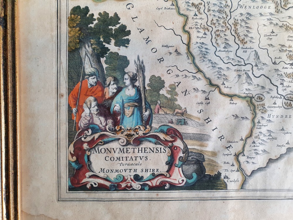 A framed 17th-century hand-coloured map of Monmouthshire featuring coats of arms, figures, a decorative cartouche, and a gilded wood frame. View IV