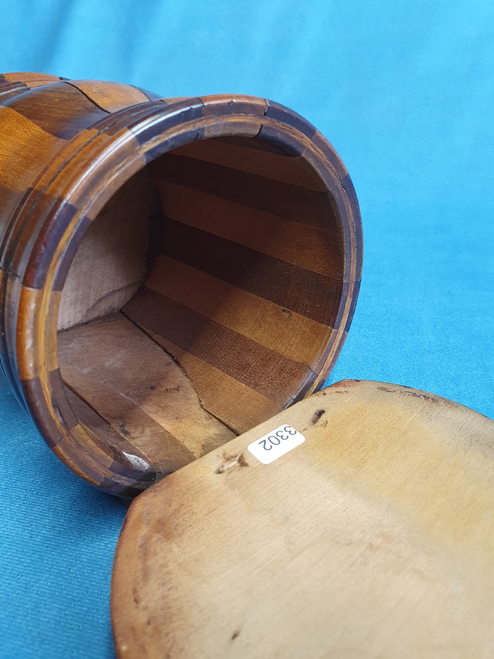 A mid-19th-century turned wooden wall-hanging salt box with staved multi-tone timber construction, a circular hinged lid, and a pierced round backboard. View IV