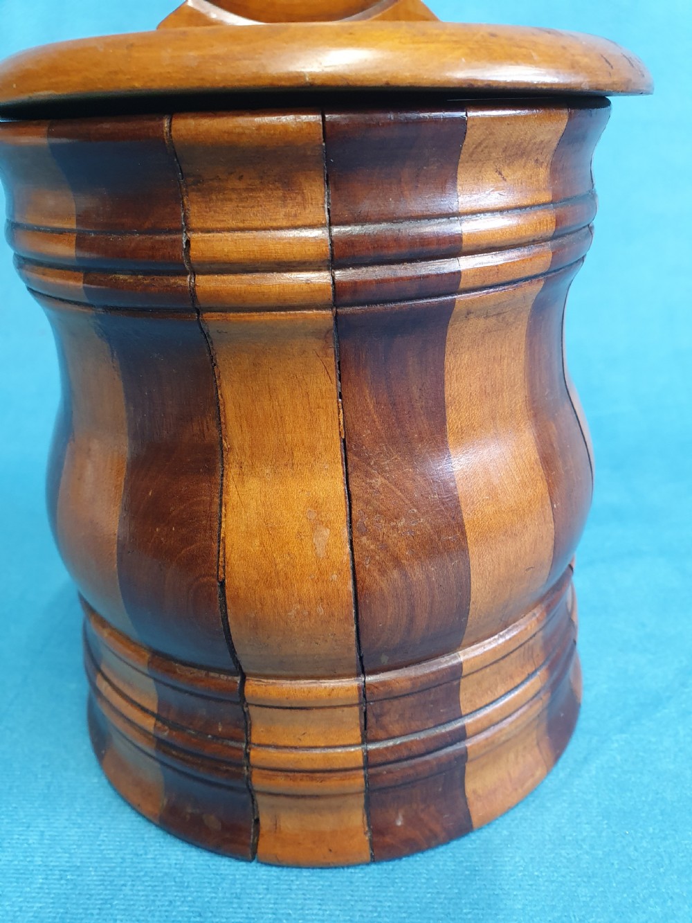 A mid-19th-century turned wooden wall-hanging salt box with staved multi-tone timber construction, a circular hinged lid, and a pierced round backboard. View V