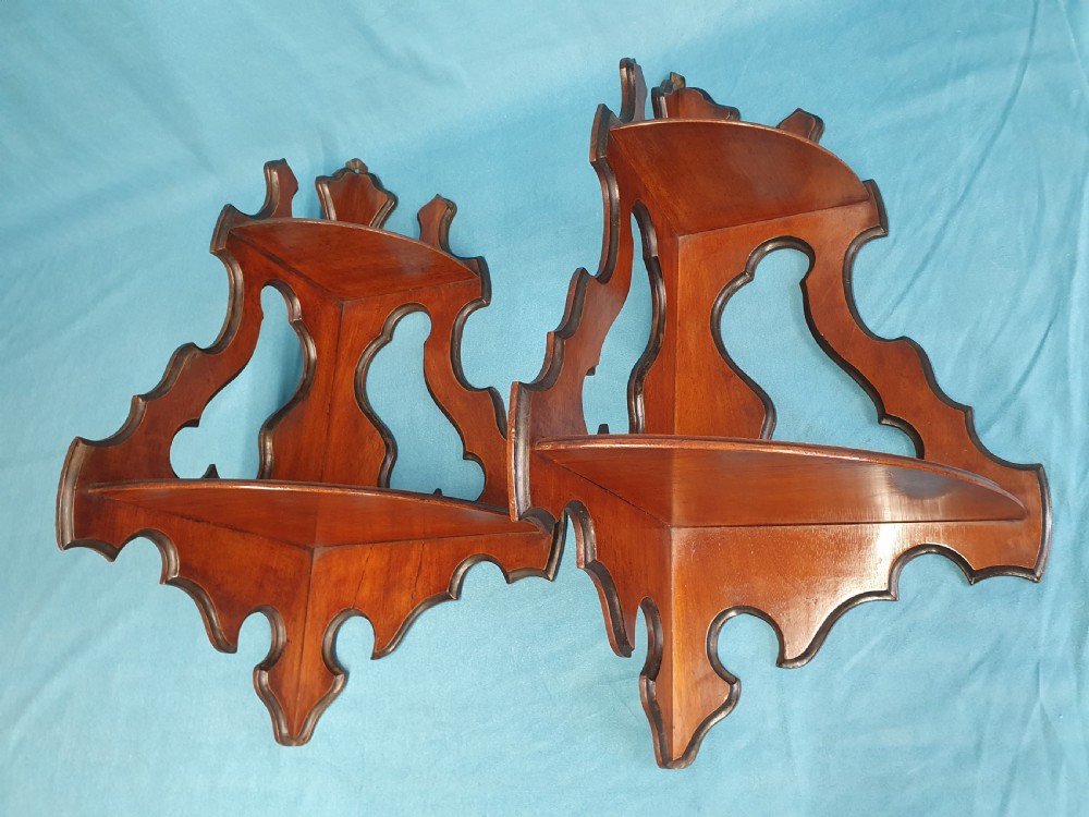 A pair of mid 19th-century mahogany corner wall brackets featuring two triangular display shelves supported by shaped scrollwork fretwork side panels.