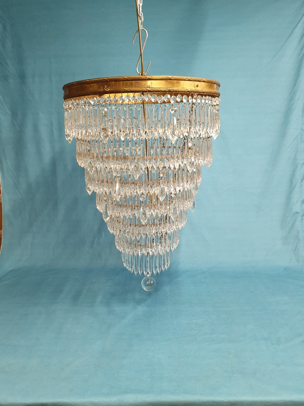A seven-tiered waterfall chandelier featuring concentric brass rings strung with elongated clear crystal spikes, ending in a single spherical glass finial. View II