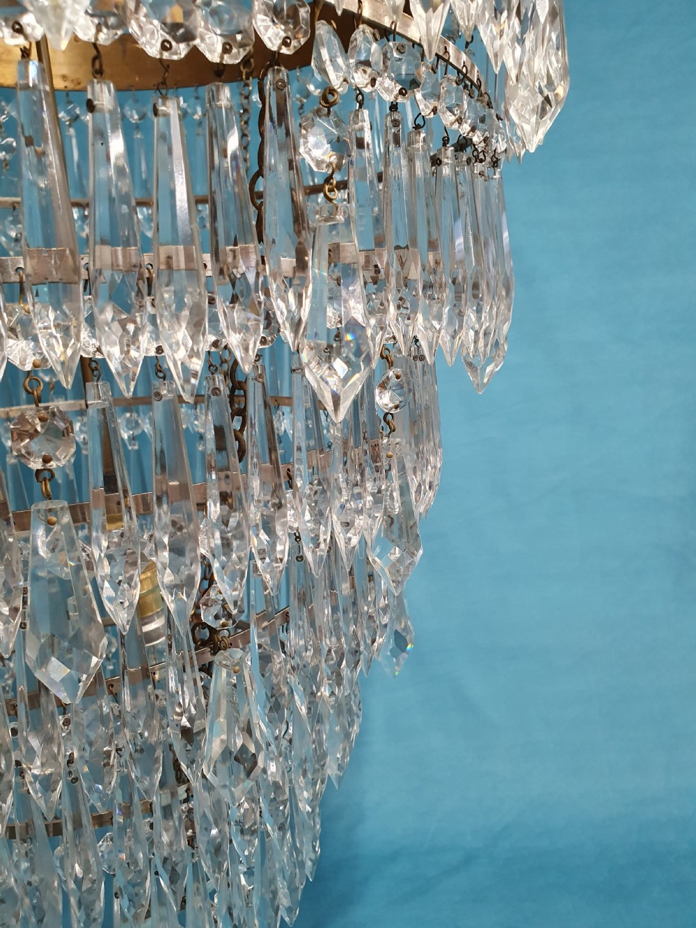 A seven-tiered waterfall chandelier featuring concentric brass rings strung with elongated clear crystal spikes, ending in a single spherical glass finial. View III