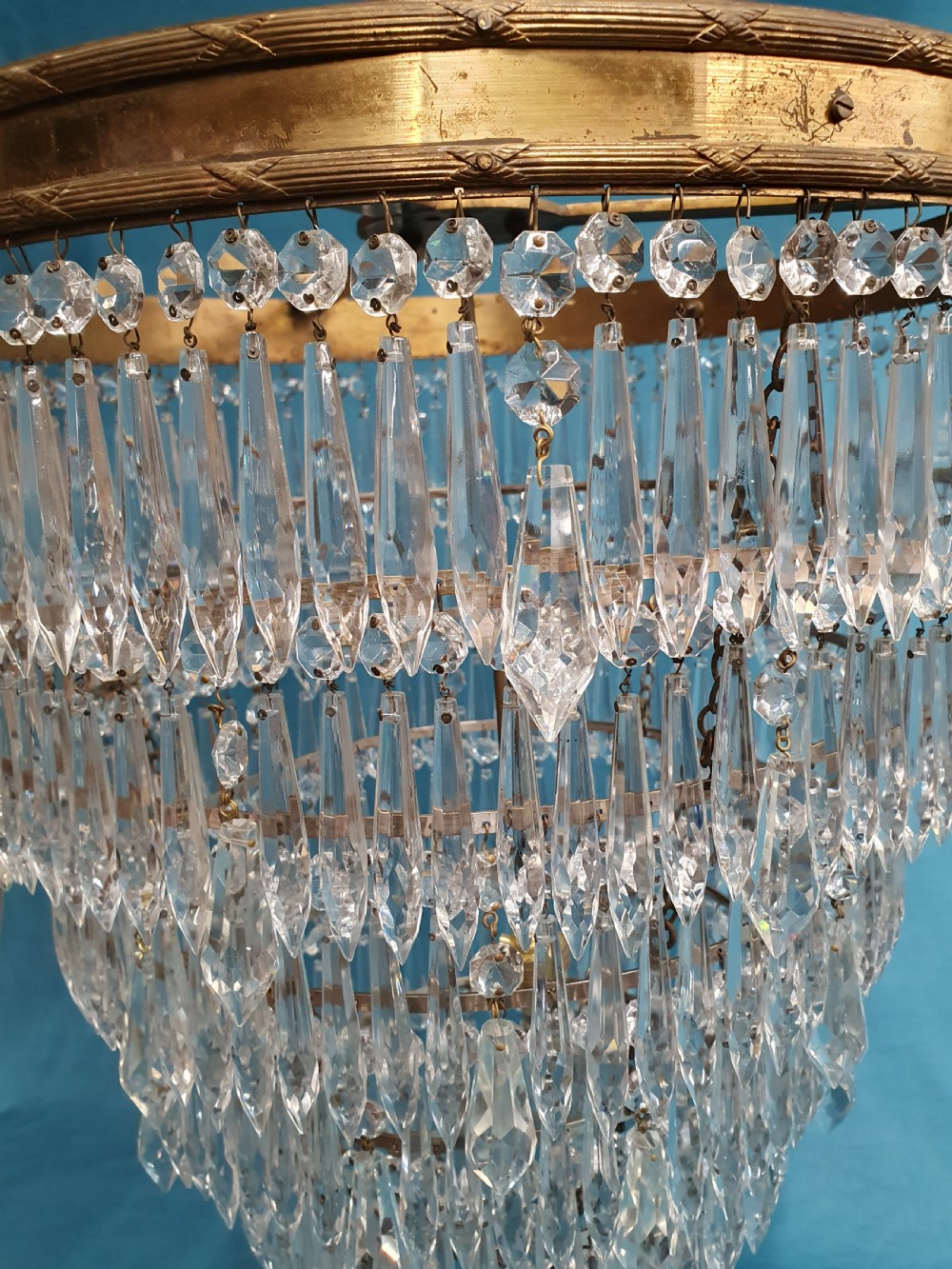 A seven-tiered waterfall chandelier featuring concentric brass rings strung with elongated clear crystal spikes, ending in a single spherical glass finial. View VI