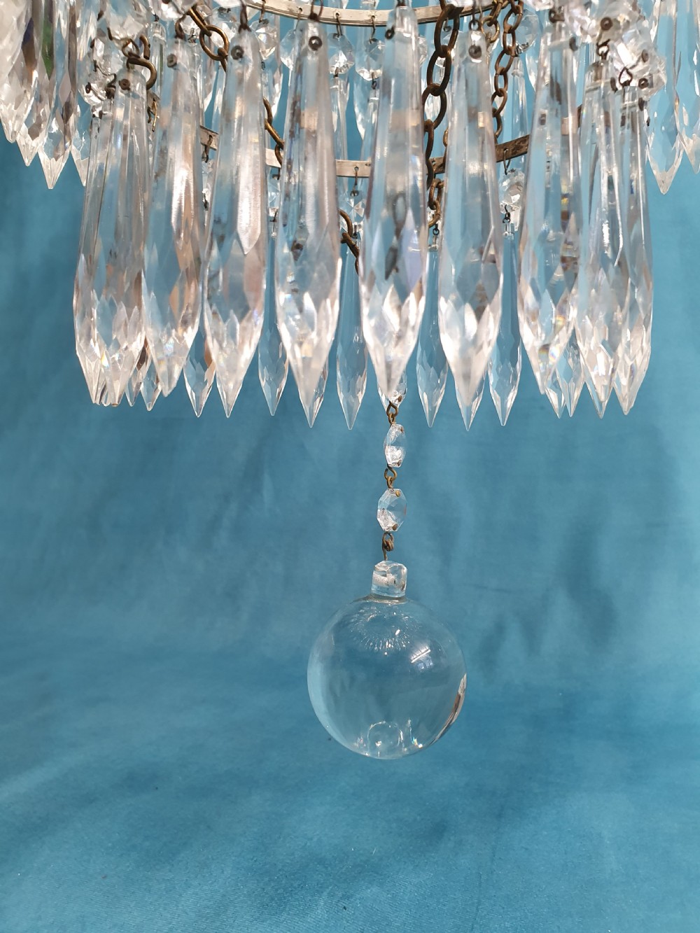 A seven-tiered waterfall chandelier featuring concentric brass rings strung with elongated clear crystal spikes, ending in a single spherical glass finial. View VIII