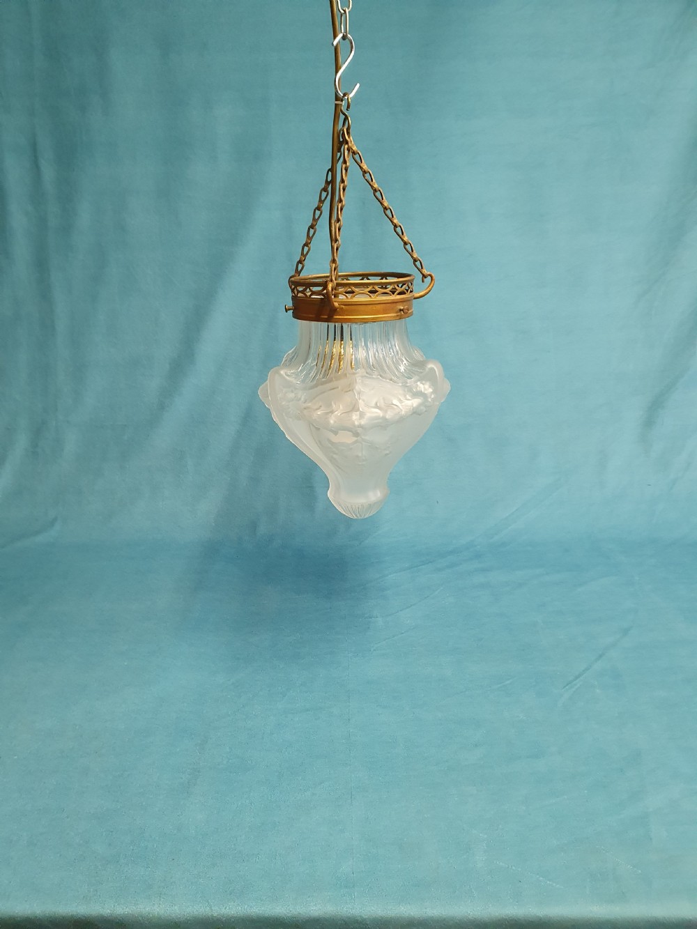 An early 20th-century glass pendant light with a frosted and moulded glass shade suspended by brass chains from a decorative brass gallery.