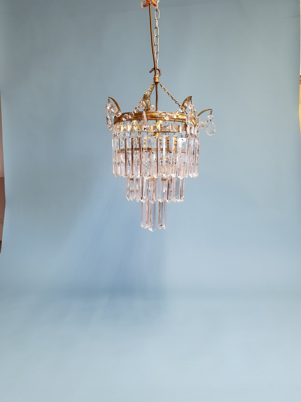 An early 20th-century tiered brass chandelier featuring rows of clear oblong crystal prisms suspended from a circular metal frame.