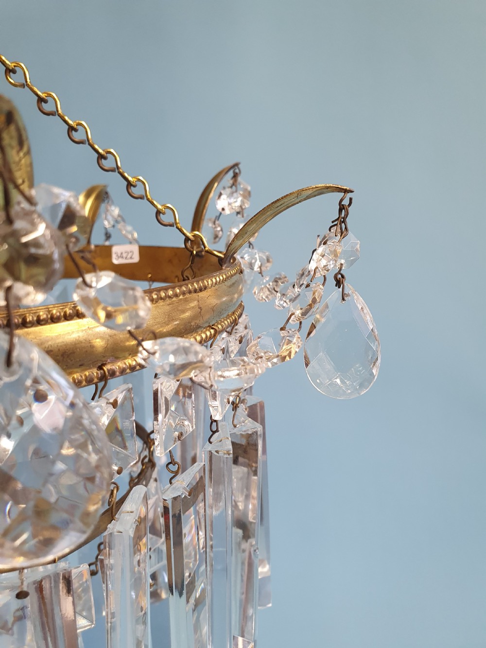 An early 20th-century tiered brass chandelier featuring rows of clear oblong crystal prisms suspended from a circular metal frame. View II