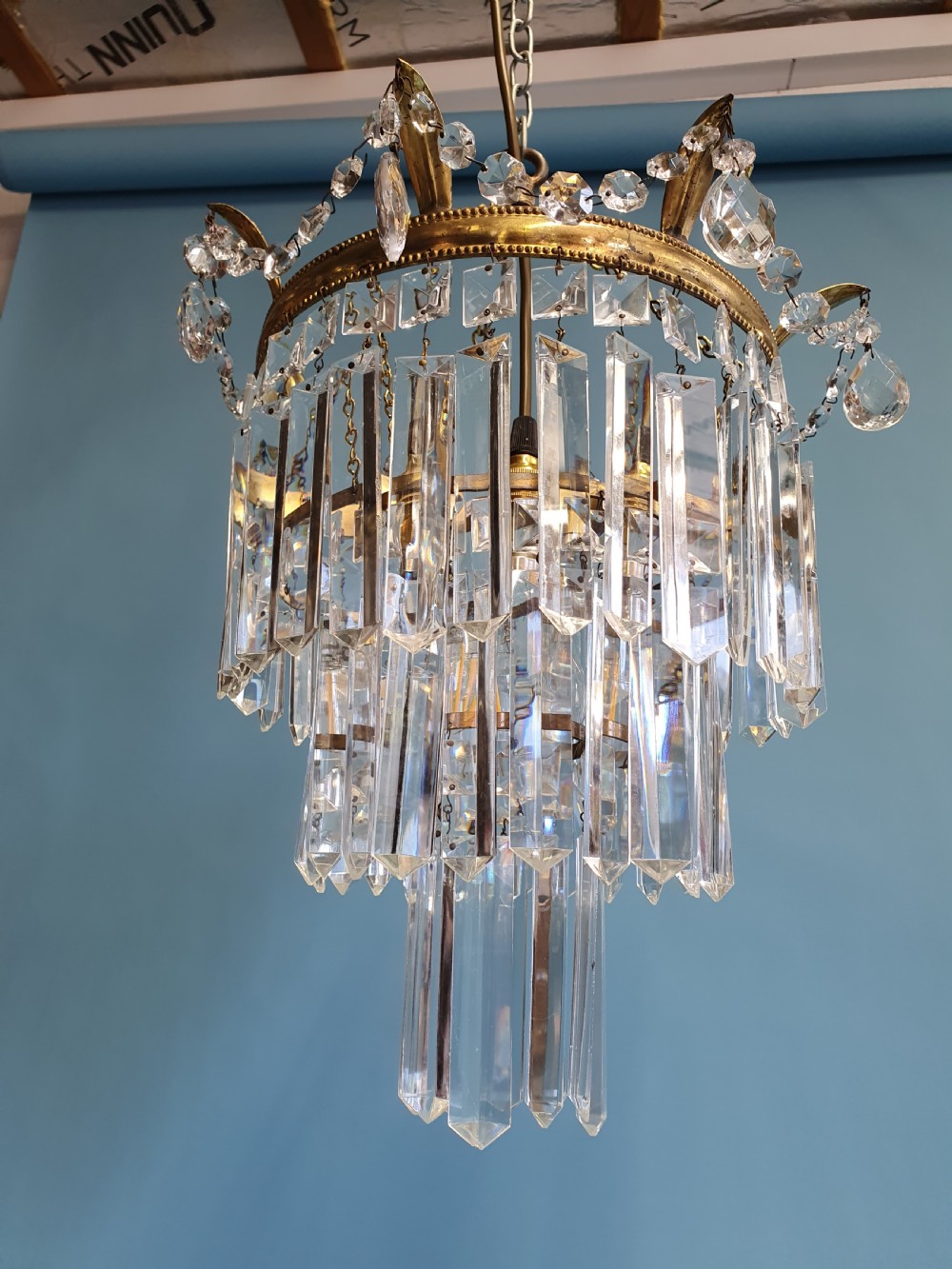 An early 20th-century tiered brass chandelier featuring rows of clear oblong crystal prisms suspended from a circular metal frame. View III