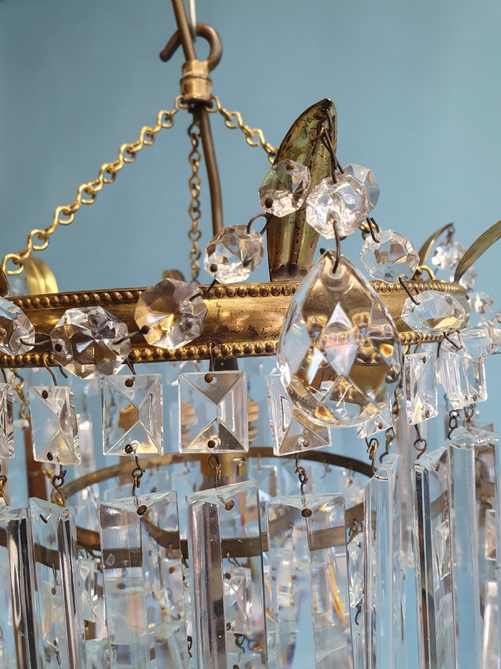 An early 20th-century tiered brass chandelier featuring rows of clear oblong crystal prisms suspended from a circular metal frame. View V