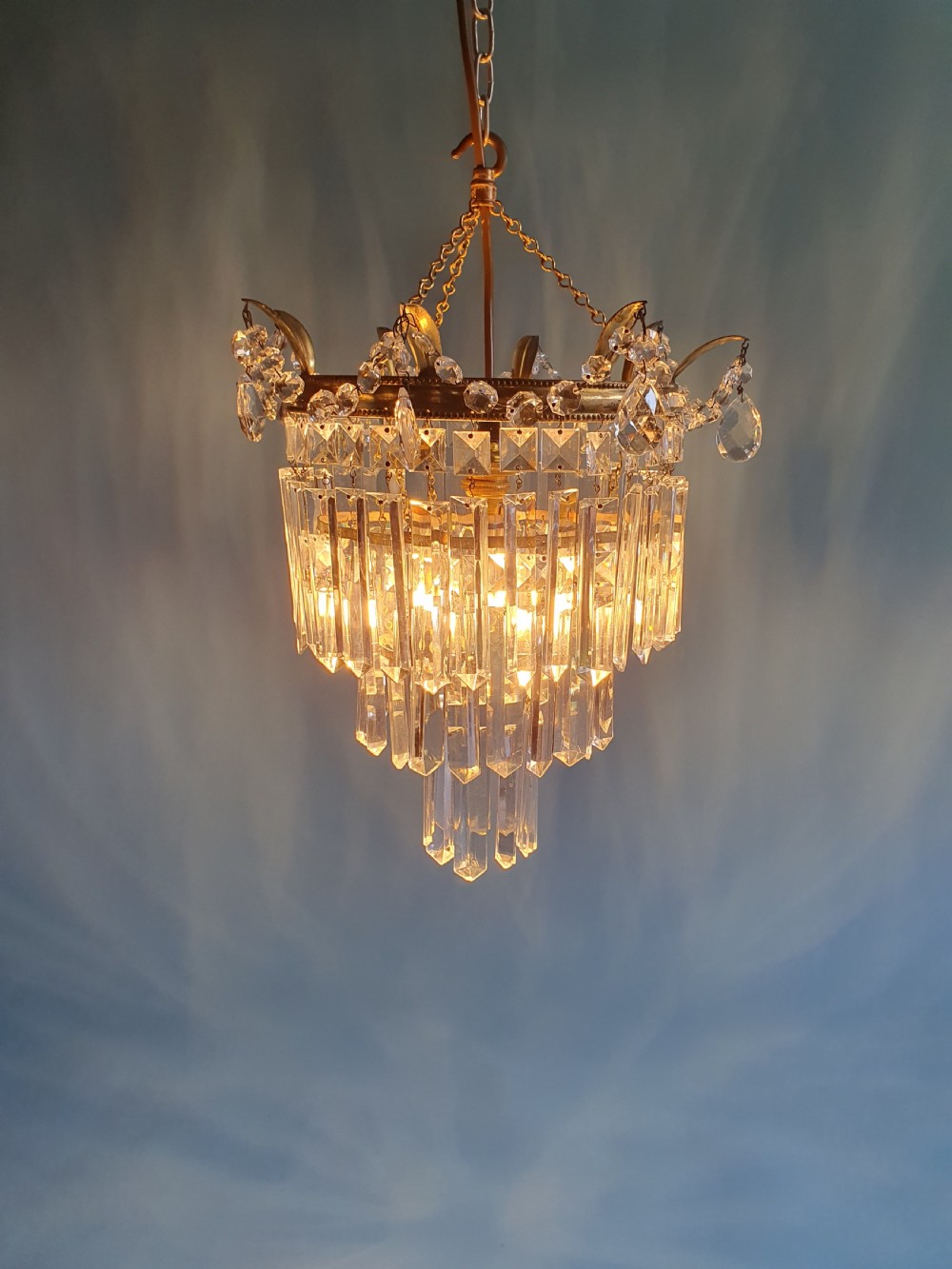 An early 20th-century tiered brass chandelier featuring rows of clear oblong crystal prisms suspended from a circular metal frame. View VI