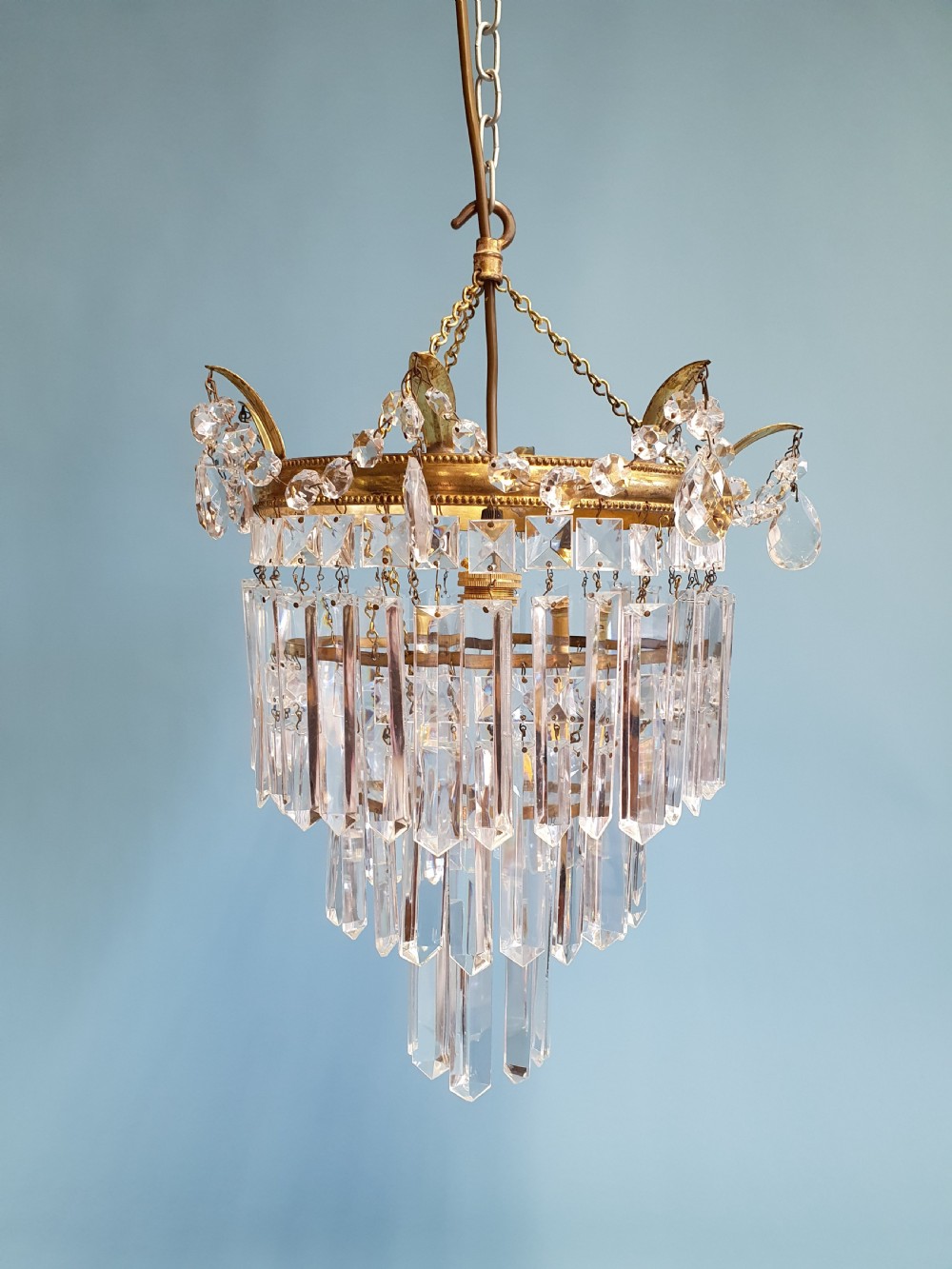 An early 20th-century tiered brass chandelier featuring rows of clear oblong crystal prisms suspended from a circular metal frame. View VII