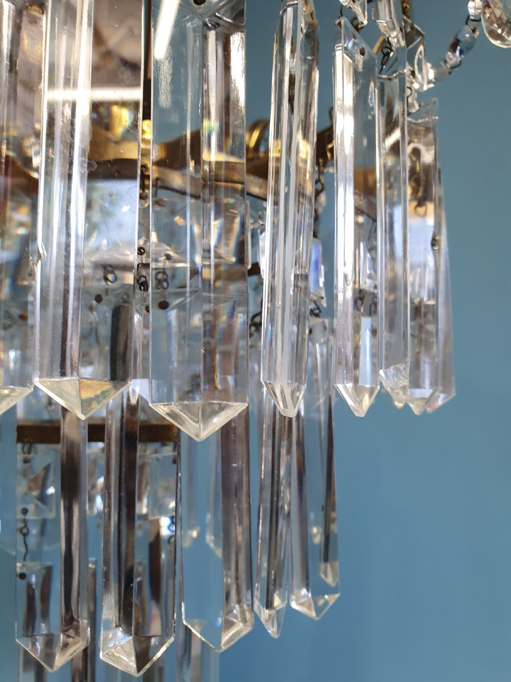 An early 20th-century tiered brass chandelier featuring rows of clear oblong crystal prisms suspended from a circular metal frame. View IX