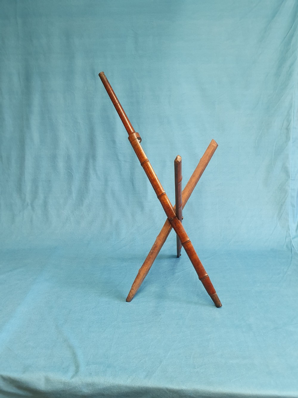 An antique cherry wood folding rod rest featuring carved faux bamboo turnings and a crossed X-frame structure.