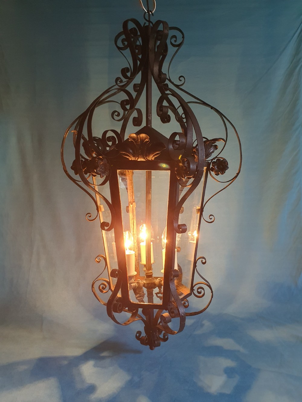 An early 20th-century wrought steel hanging porch lantern featuring elaborate scrollwork, leaf accents, clear glass panels, and an internal multi-bulb light fitting. View IV