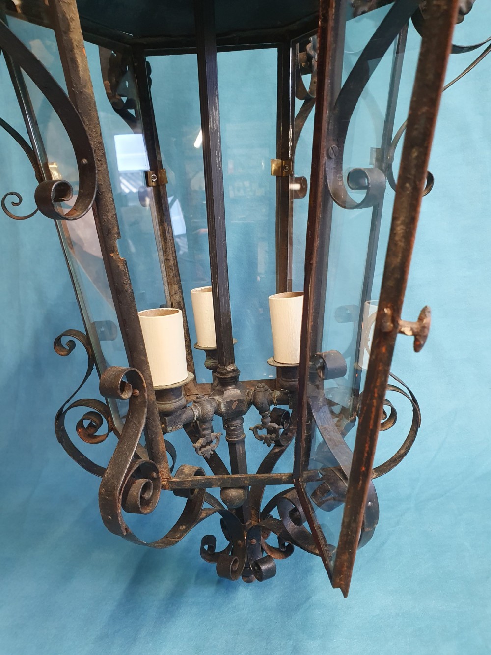 An early 20th-century wrought steel hanging porch lantern featuring elaborate scrollwork, leaf accents, clear glass panels, and an internal multi-bulb light fitting. View V