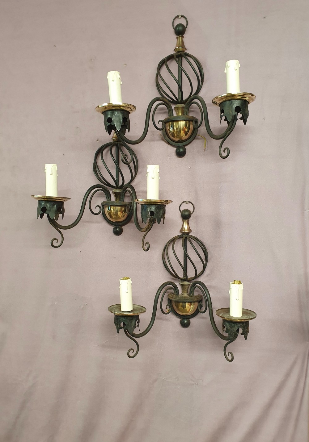 A trio of early twentieth-century dark steel twin-arm wall sconces featuring openwork twisted central cages, scrolled arms, and polished brass accents.