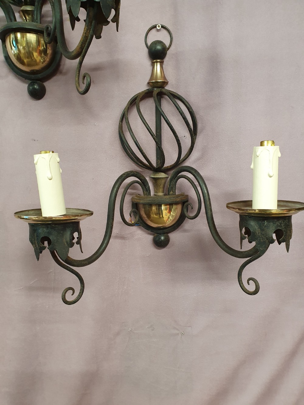 A trio of early twentieth-century dark steel twin-arm wall sconces featuring openwork twisted central cages, scrolled arms, and polished brass accents. View II