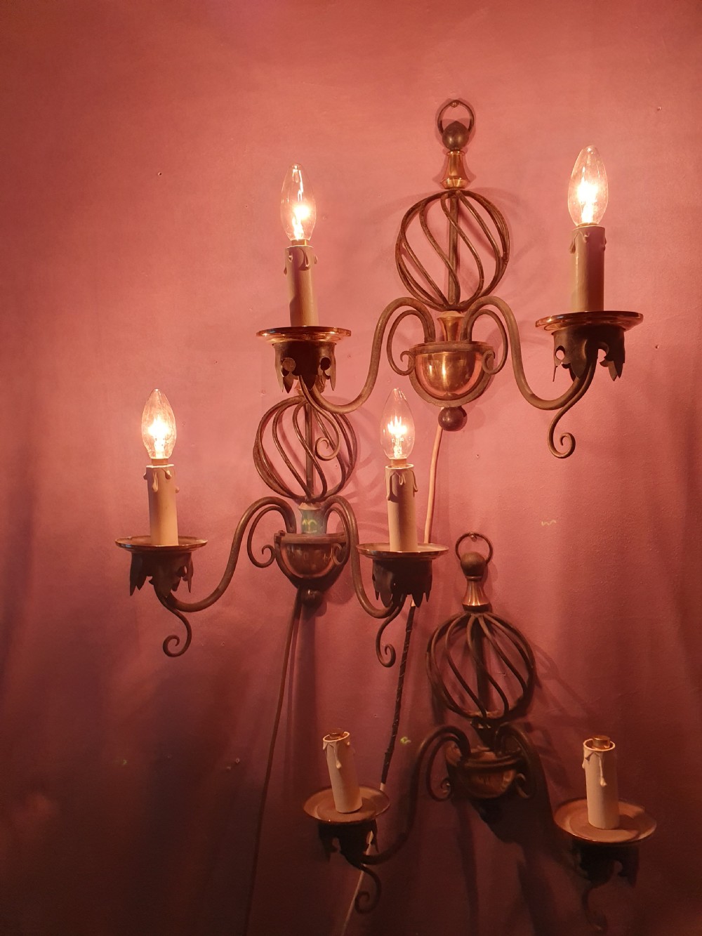 A trio of early twentieth-century dark steel twin-arm wall sconces featuring openwork twisted central cages, scrolled arms, and polished brass accents. View VI