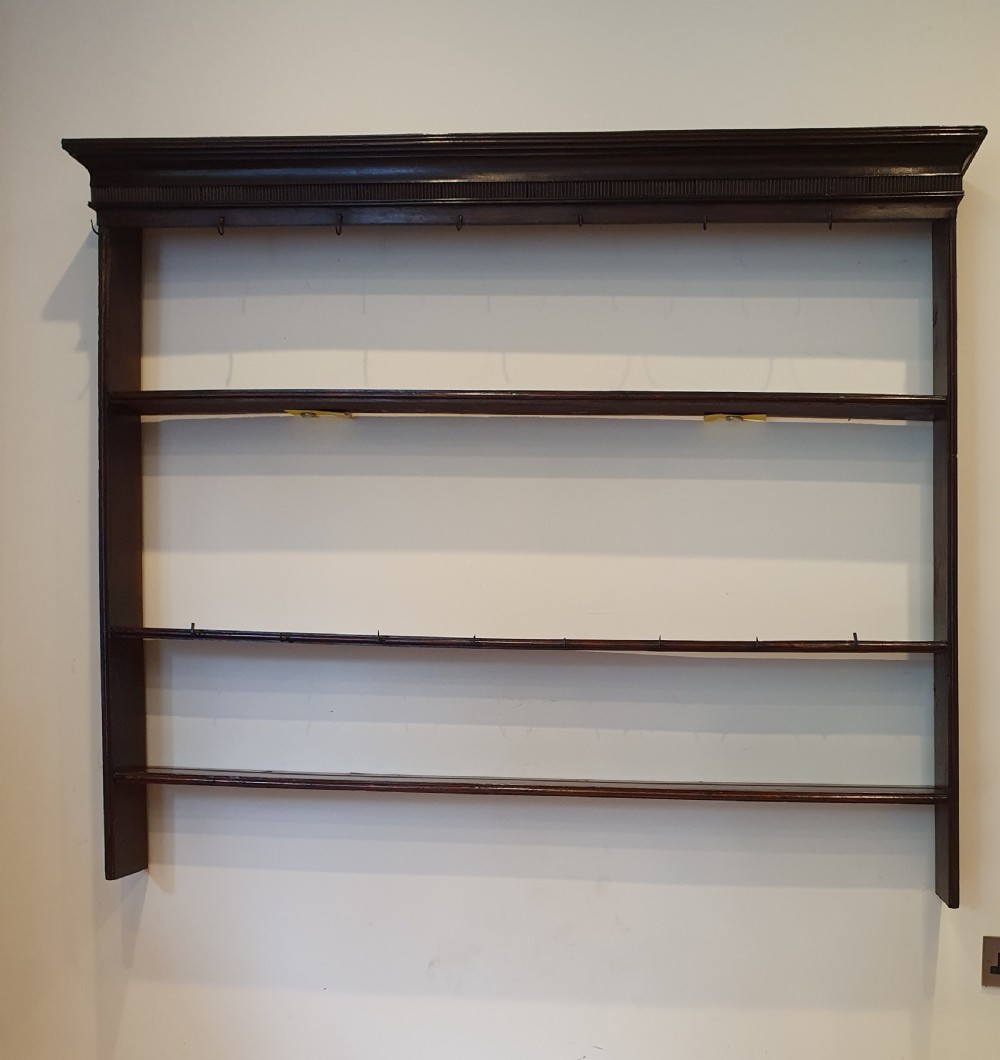 Dark oak early eighteenth-century dresser rack featuring a projecting moulded cornice, three open shelves, and small metal cup hooks.