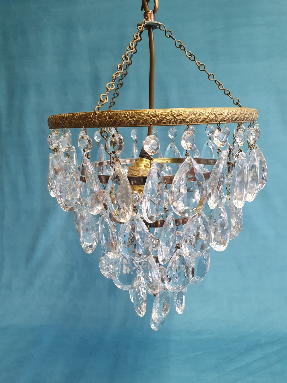 An early 20th-century ceiling light featuring an embossed brass ring with cascading tiers of teardrop-shaped glass crystals hanging from three brass chains.