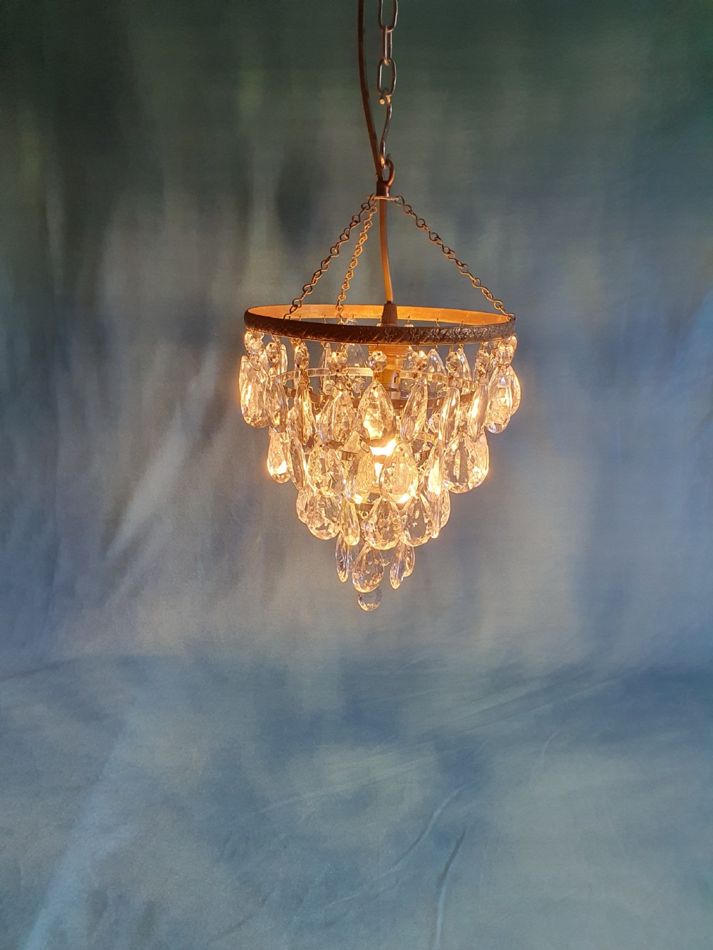 An early 20th-century ceiling light featuring an embossed brass ring with cascading tiers of teardrop-shaped glass crystals hanging from three brass chains. View V
