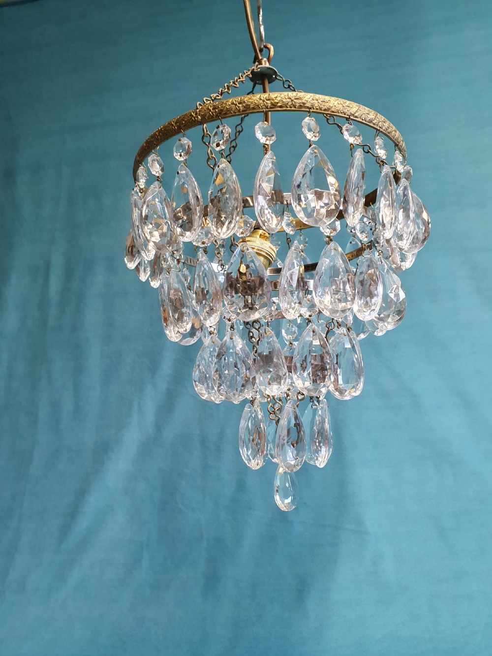 An early 20th-century ceiling light featuring an embossed brass ring with cascading tiers of teardrop-shaped glass crystals hanging from three brass chains. View VII