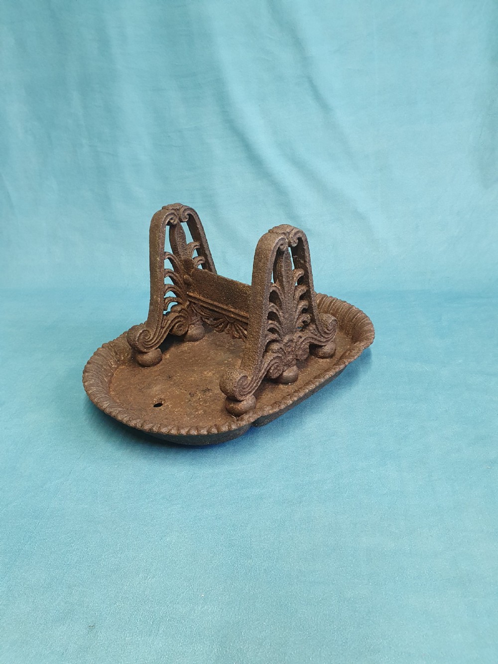 A 19th-century cast iron boot scraper featuring a dished oval tray base and two ornate scrollwork side supports holding a central scraping blade.