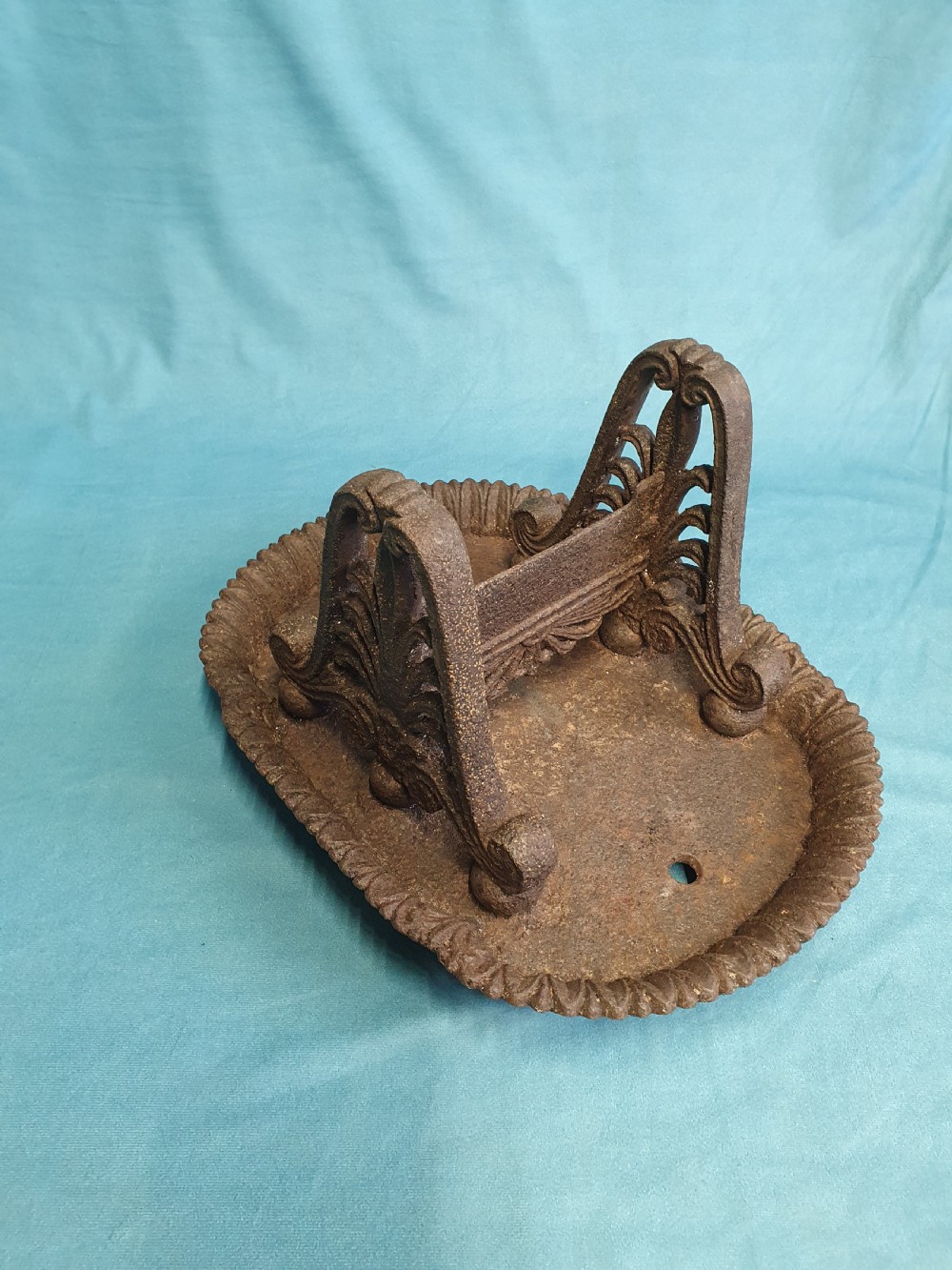 A 19th-century cast iron boot scraper featuring a dished oval tray base and two ornate scrollwork side supports holding a central scraping blade. View VI