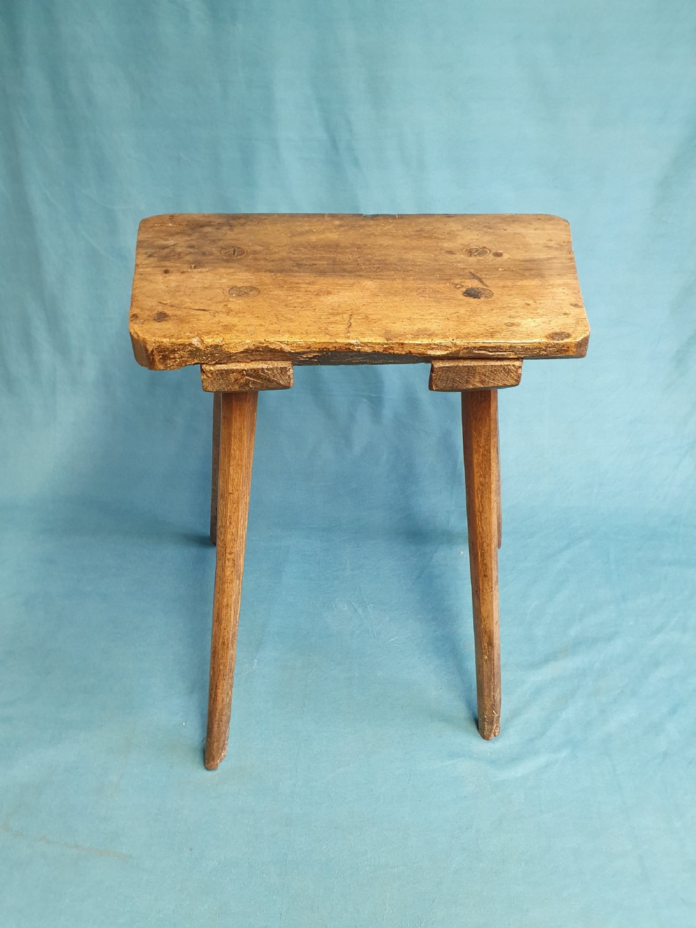 A late 19th-century walnut stick stool featuring a rectangular thick wooden seat raised on four round splayed legs.