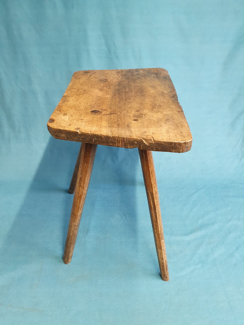 A late 19th-century walnut stick stool featuring a rectangular thick wooden seat raised on four round splayed legs. View V