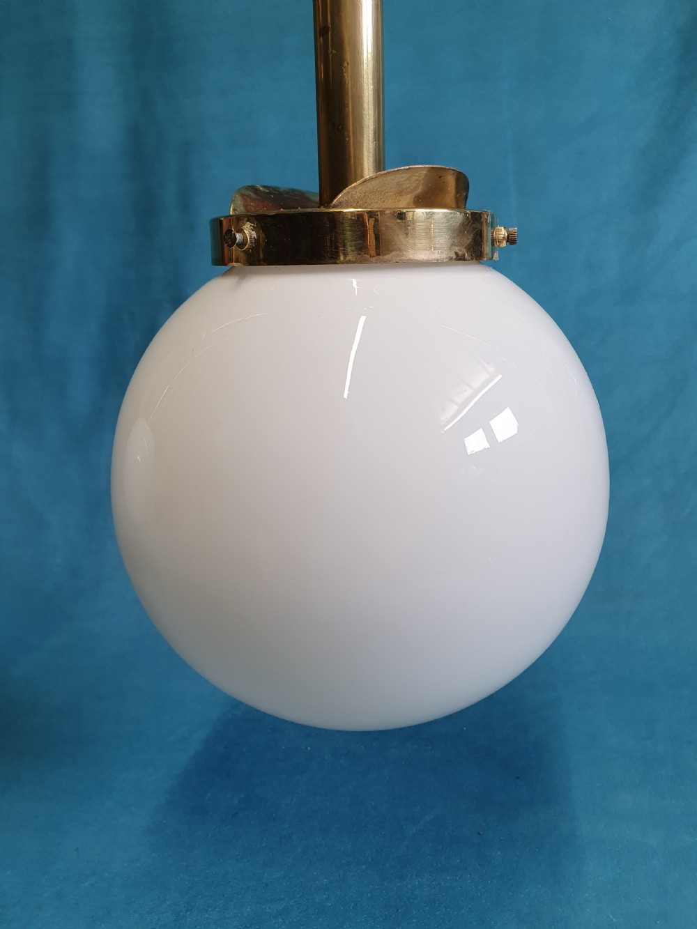 An early twentieth-century brass pendant light fixture featuring a horizontal bar suspended by dual brass chains, holding two spherical white glass globes with scrollwork detailing. View V