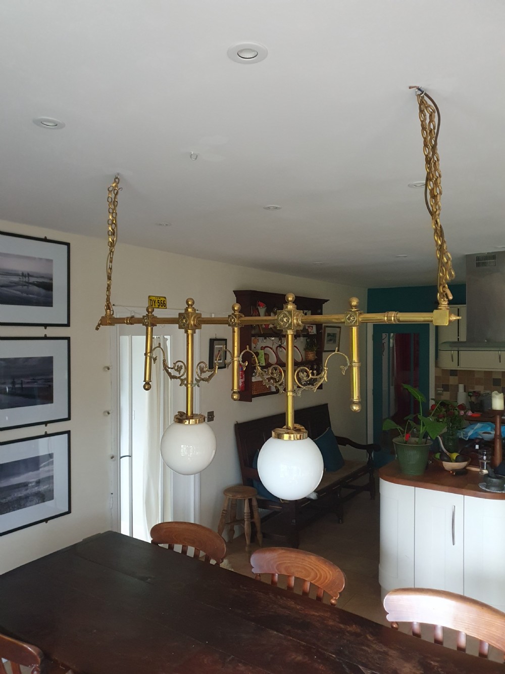 An early 20th-century Gothic Revival linear brass chandelier featuring a horizontal bar structure with ornate scrollwork brackets and two suspended white opaline glass globes.