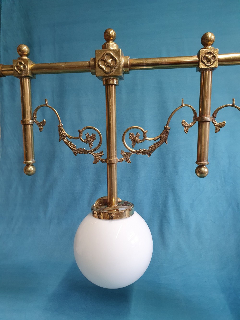 An early 20th-century Gothic Revival linear brass chandelier featuring a horizontal bar structure with ornate scrollwork brackets and two suspended white opaline glass globes. View VII