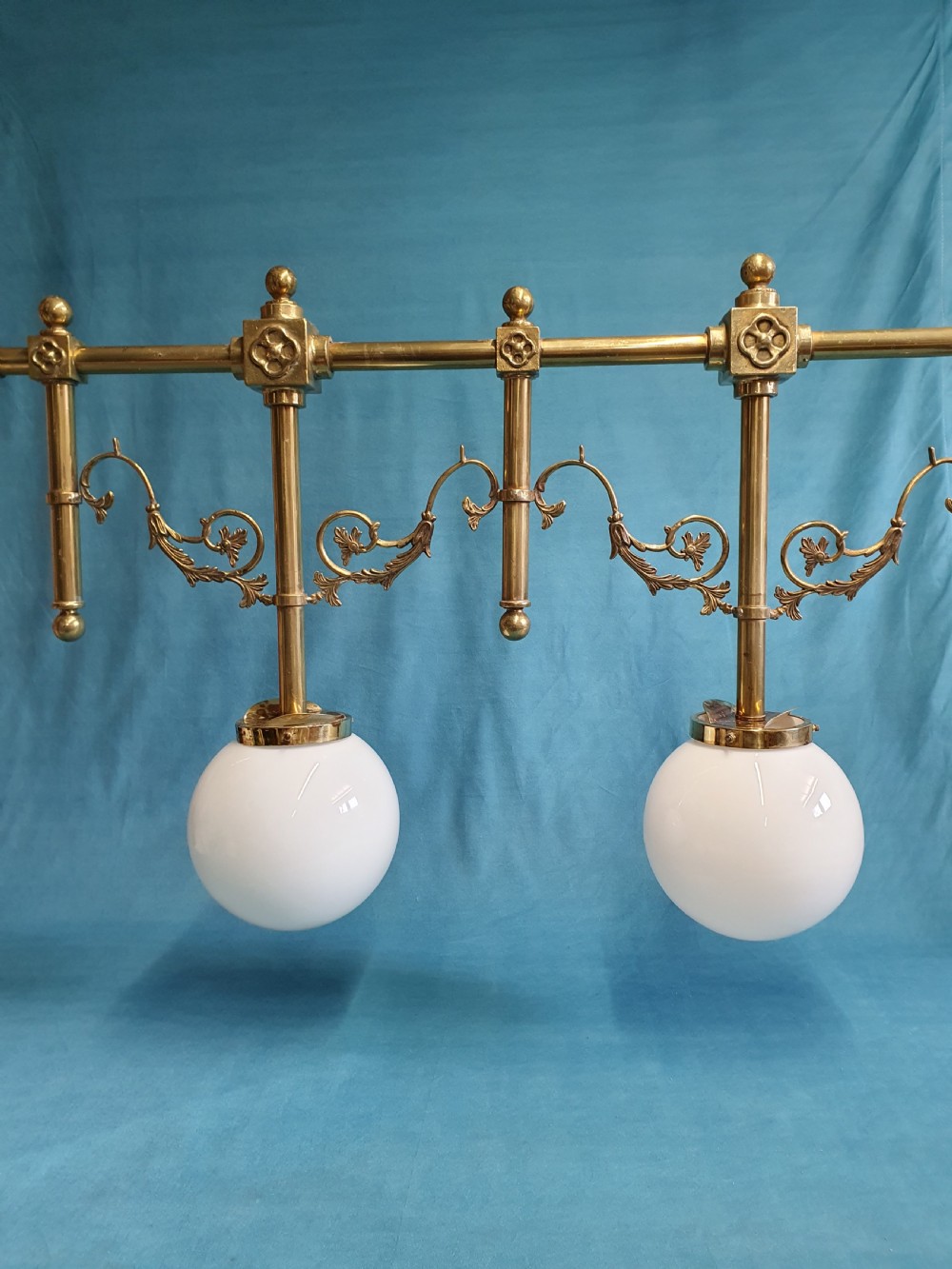 An early 20th-century Gothic Revival linear brass chandelier featuring a horizontal bar structure with ornate scrollwork brackets and two suspended white opaline glass globes. View VIII