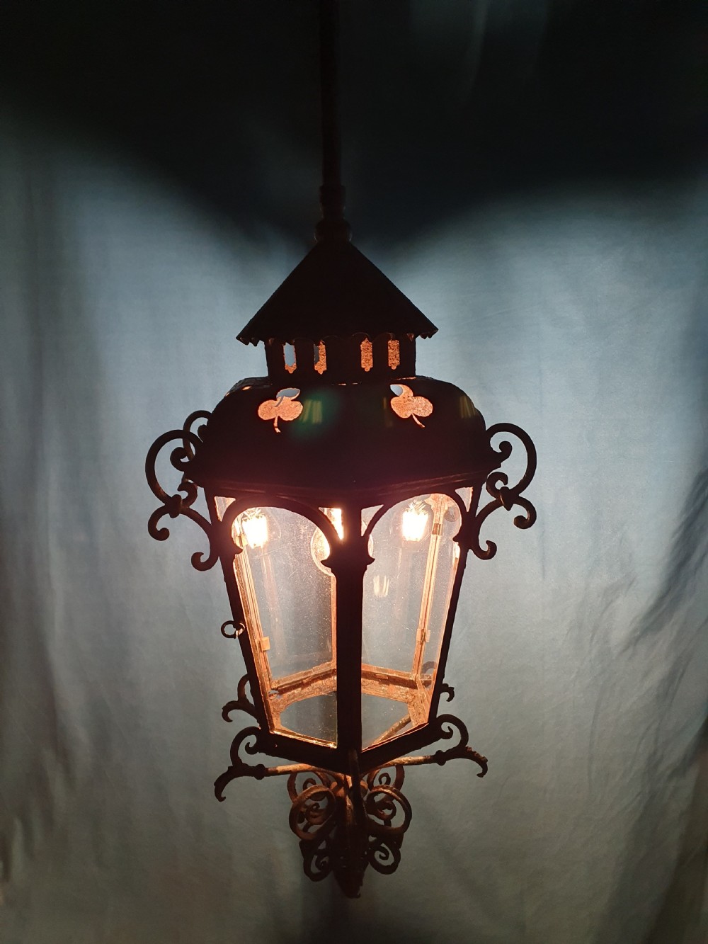 A late 19th-century wrought iron hanging lantern featuring decorative scrollwork, shamrock cutouts along the top canopy, and clear glass side panels. View VI