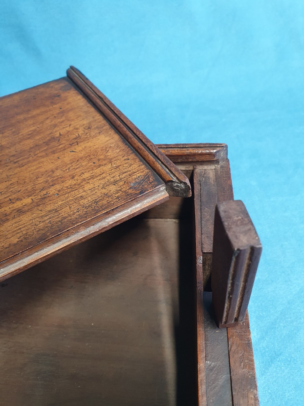 Close-up view of a small open mahogany box with a wooden spring catch mechanism along the rim.