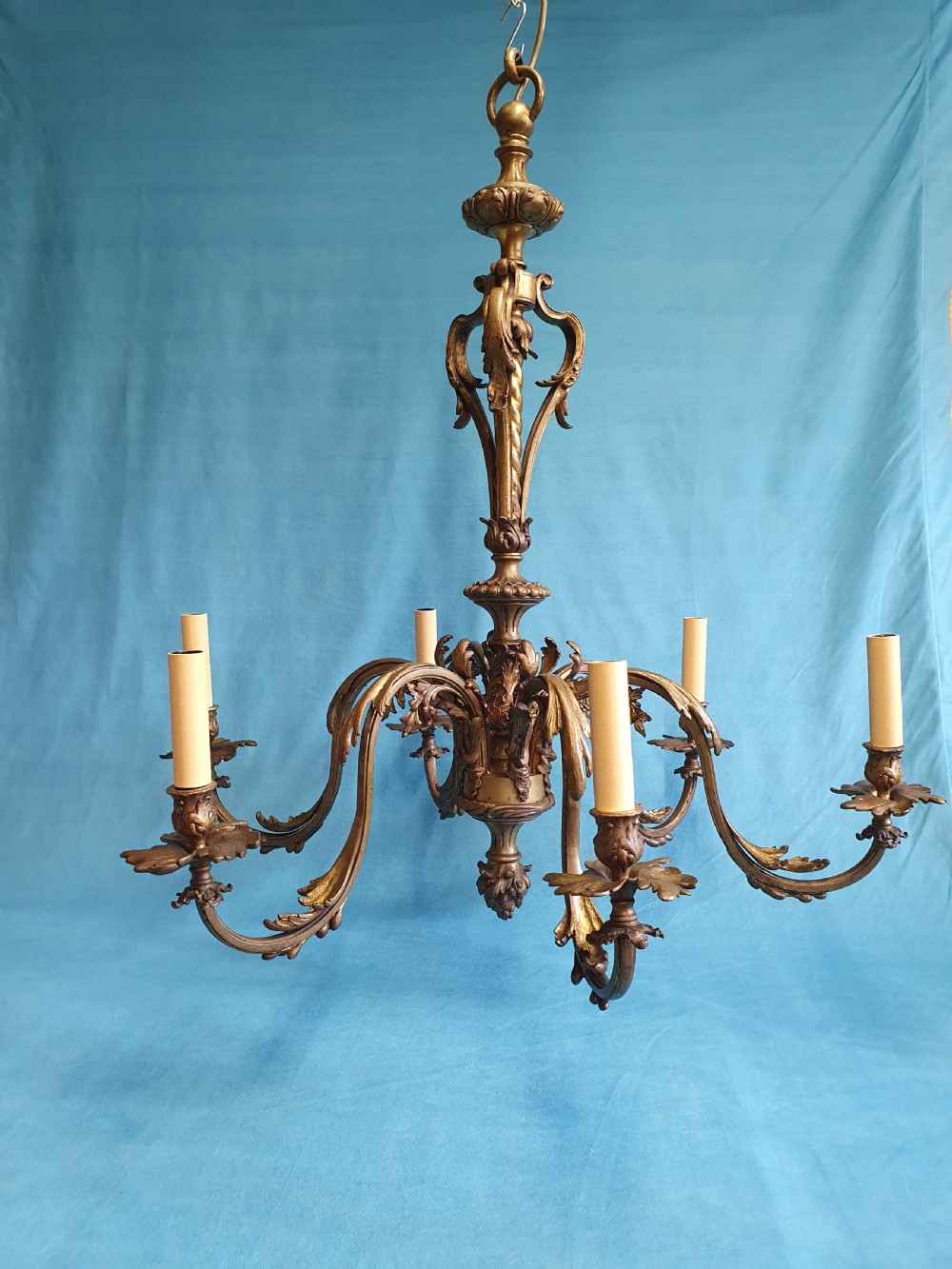 A six-arm cast brass French chandelier featuring scrollwork branches, central acanthus leaf detailing, and small white pleated fabric lampshades. View III