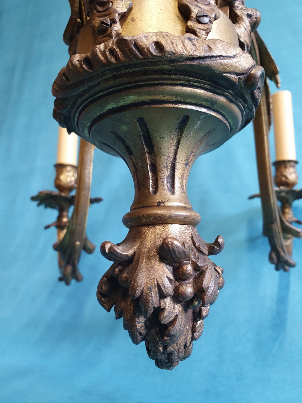 A six-arm cast brass French chandelier featuring scrollwork branches, central acanthus leaf detailing, and small white pleated fabric lampshades. View VIII
