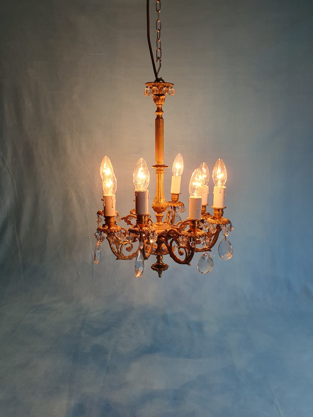 An eight-arm brass ceiling chandelier featuring candle-effect light fittings and suspended crystal glass drops. View VIII