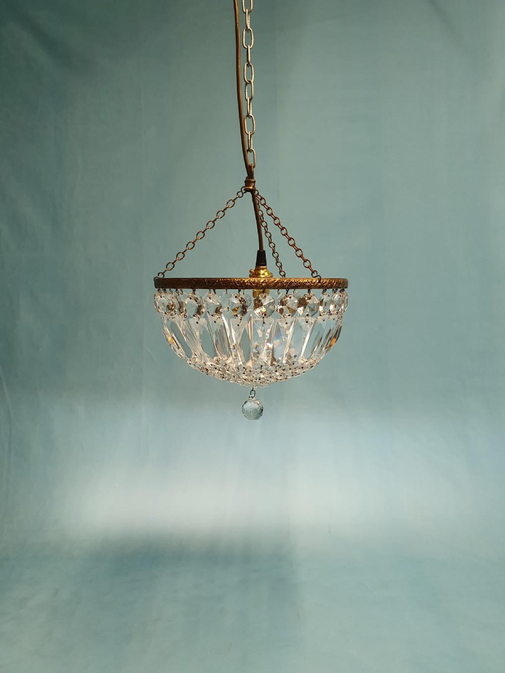 An early 20th century ceiling chandelier featuring a circular brass frame with suspended cut crystal prisms forming a hemispherical bag structure.