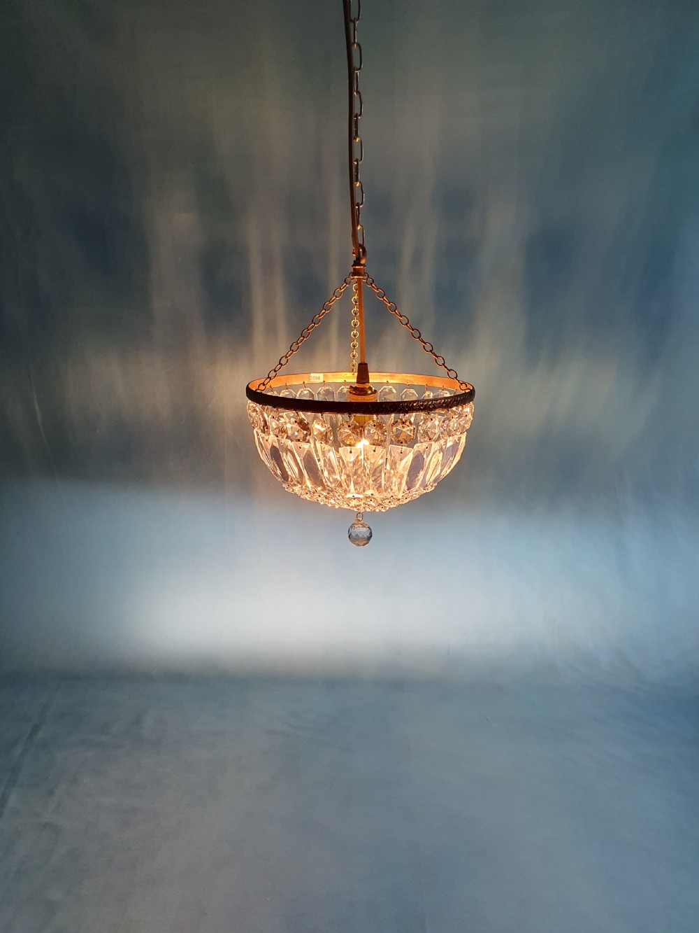 An early 20th century ceiling chandelier featuring a circular brass frame with suspended cut crystal prisms forming a hemispherical bag structure. View VI