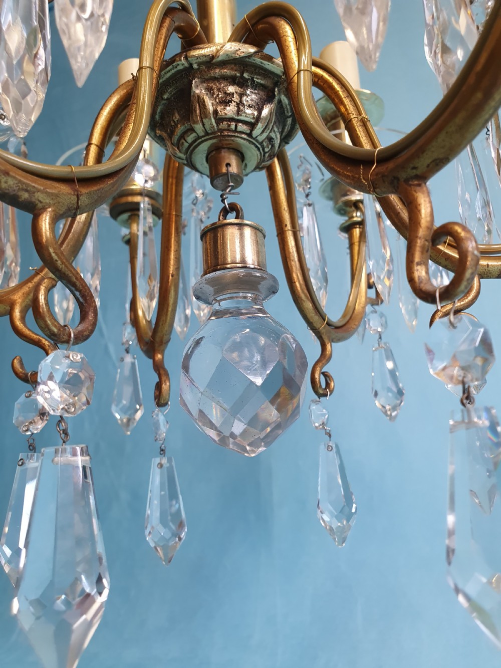 A small six-arm brass chandelier featuring glass drip pans, hanging faceted crystal drops, and a central brass stem with a suspension chain. View III