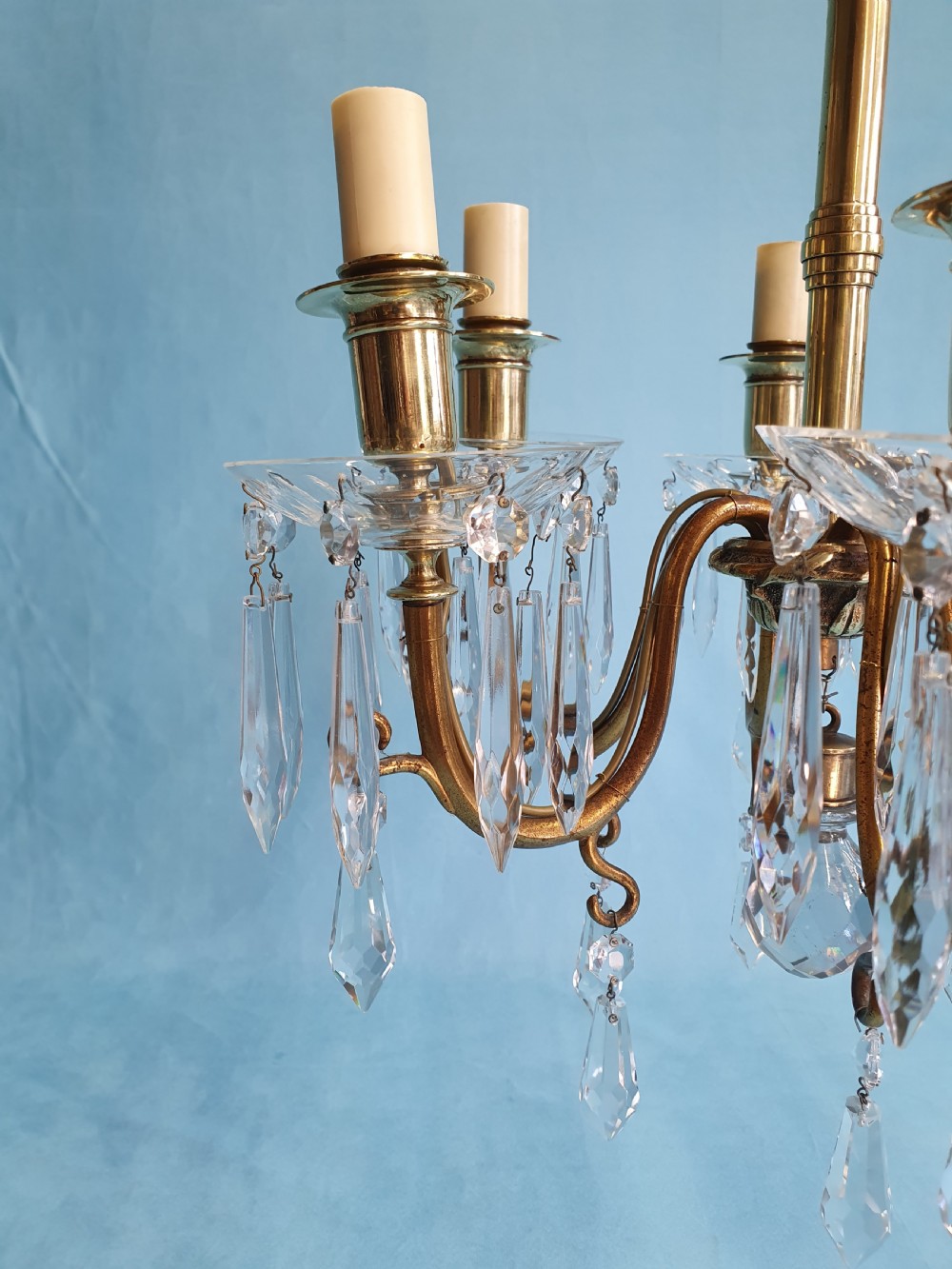 A small six-arm brass chandelier featuring glass drip pans, hanging faceted crystal drops, and a central brass stem with a suspension chain. View V